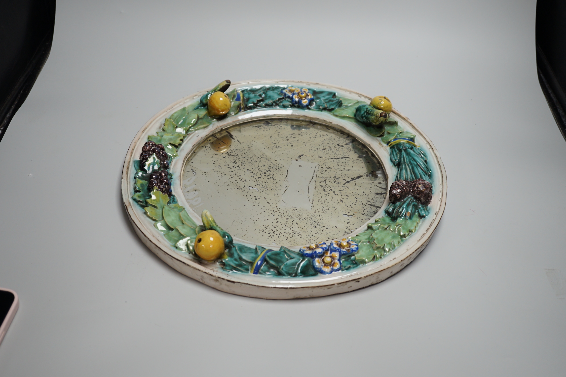 A circular earthenware mirror, possibly by Della Robbia Pottery of Liverpool, decorated with foliage and fruit, 37cm